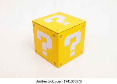 Ảnh tĩnh vật trong nhà của một chiếc hộp màu vàng có in một dấu chấm hỏi lớn màu trắng trên mỗi mặt. Nó gợi lại yếu tố đồ họa của một trò chơi điện tử nền tảng nổi tiếng.