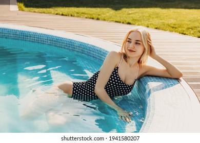 Jeune femme blonde, portant un maillot de bain une pièce à pois, assise dans une piscine par une journée ensoleillée, se relaxant.