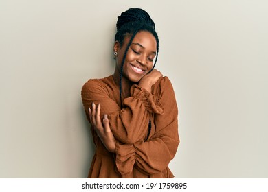 African american woman with braided hair wearing casual brown shirt hugging oneself happy and positive, smiling confident. self love and self care 