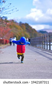 Un niño asiático con una chaqueta de invierno haciendo la carrera de Naruto, inclinado hacia adelante con los brazos extendidos hacia atrás, hacia la cámara, en el lago Yamanaka, Japón