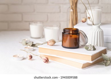 Home decoration and interior. Beautiful burning candles with eucalyptus leaves and dry flowers on pile of white books