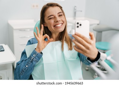 Happy young woman taking a selfie during medical checkup at dentist's cabinet, ok