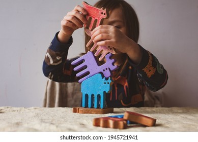 thuisonderwijs, vrijeschoolonderwijs, een balans leren - meisje bouwt een balanstoren van gekleurd houten speelgoed: bizon, eland, vos en lynx