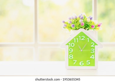 Green clock tells time 11.00 a.m. with flower vase on white table by the window glass blurred green background.