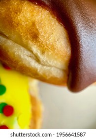 Пончик або пончик: крупним планом або макрознімок пончика Boston Cream з шоколадною глазур’ю на передньому плані з жовтою глазур’ю та райдужними круглими бризками з розмитим фокусом на задньому плані.
