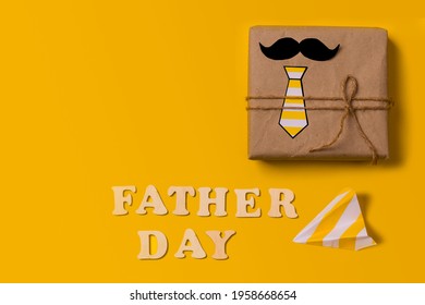 Geschenkdoos op een gele achtergrond met de inscriptie in houten letters Vaderdag. Plat leggen. Vaderdag cadeau aan papa. Happy Father's Day-vakantieconcept in 2021. Kopieer de ruimte