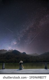 Silhueta de uma mulher asiática sentada sozinha à beira do lago. Sentindo falta do seu amor e imaginando a atmosfera noturna com as estrelas e a Via Láctea, ela se sente feliz. Longa exposição, com granulação.