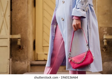 Street style, fashion details: small pink faux patent leather baguette bag in trendy outfit. Woman holding mini handbag. Copy, empty space for text