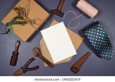 Vatertags- oder männliche Geburtstagsgrußkarten-Einladung im Flatlay-Stil mit Geschenk, Schokoladen-Werkzeugset und Krawatte. Weißes Produktmodell mit negativem Kopienraum für Ihren Text oder Design hier.