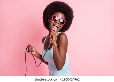 Foto van een gelukkige jonge vrouw met een donkere huid, houdt zingende mic-muziekliefhebber geïsoleerd op een roze achtergrond