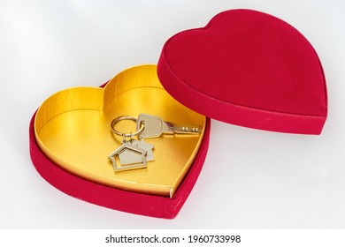 Conceito de compra de imóveis e casas como um presente de dia dos namorados. Caixa em forma de coração dentro da chave da casa em fundo branco isolado.