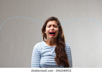 Traurige emotionale junge Frau, die reichlich Tränen schluchzt und vor Qual und Trauer über einem grauen Studiohintergrund jammert