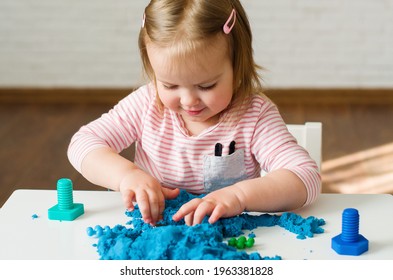 Little girl playing with blue kinetic sand. Educational games with children for fine motor skills. Sand therapy indoors. Concept of sensory and creativity game, therapy hand, development of fine motor