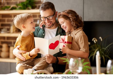 Wir lieben dich, Papa. Junger glücklicher Vater, der zum Vatertag von zwei aufgeregten Kindern zu Hause, Sohn und Tochter, gratuliert, lächelnde Kinder, die Papa eine handgemachte Postkarte und eine verpackte Geschenkbox geben