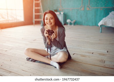 Indoor fashion portrait of pretty young brunette girl sitting on the floor and taking picture on vintage retro old school camera