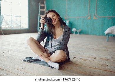 Indoor fashion portrait of pretty young brunette girl sitting on the floor and taking picture on vintage retro old school camera
