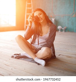 Indoor fashion portrait of pretty young brunette girl sitting on the floor and taking picture on vintage retro old school camera