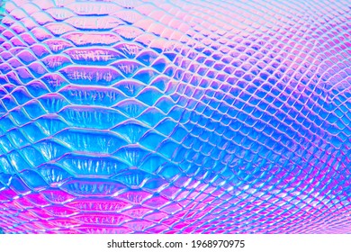 Abstrakter Hintergrund mit holographischem hellem mehrfarbigem Regenbogen. Metallisiertes Makro aus nächster Nähe. Nachahmung der Regenbogenfarbe. Hintergrund mit einer Reptilienhautstruktur in rosa und blau getönt.