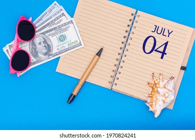 hari ke 4 juli. Konsep perjalanan flat lay - notepad dengan pena tanggal 4 juli, kacamata, dolar dan kerang di latar belakang biru. Bulan musim panas, konsep hari dalam setahun.