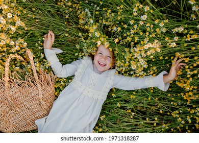 una niña feliz con un vestido de algodón yace en un campo de margaritas en verano al atardecer. risas, vista desde arriba