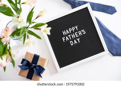 Glückliches Vatertagskonzept. Briefbrett mit Text Happy Father's Day, Krawatte, Geschenkbox, Blumenstrauß auf dem Tisch. Flache Lage, Draufsicht, Overhead