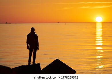 Woman or man standing on rock looking straight. Nature and beauty concept. Orange sundown. Girl silhouette at sunset