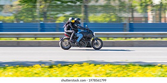Mand og kvinde kører på en sort motorcykel i høj fart på en asfaltvej i forgrunden af ​​gule mælkebøtter. Rejse- og sportskoncept, hastighed og frihed.