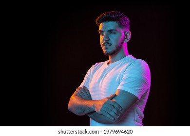 Hands crossed, confidence. Latino young man's portrait on black studio background in neon light. Handsome male model. Concept of human emotions, facial expression, youth, sales. Copy space for ad.