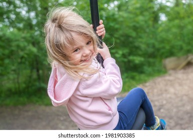 Klein meisje rijdt op speeltoestellen van Flying Fox. Kind meisje lacht in een kinderspeelplaats. Zomertijd.