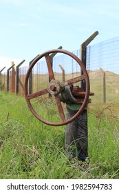 Alte verlassene Getriebeventilspindel und Griff im grünen Gras vor einem alten Stacheldrahtzaun und blauem Himmel