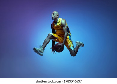 In beweging. Portret van atletiese Afro-Amerikaanse manlike basketbalspeler wat in neonlig op blou agtergrond geïsoleer is. Konsep van gesondheid, professionele sport, stokperdjie. Passievol, modieus