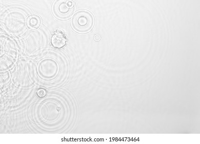 彩度の低い透明な澄んだ穏やかな水面のテクスチャーと波紋、水しぶき 抽象的な自然の背景。日光の下で白灰色の水の波 コピースペース 化粧品 保湿剤 ミセルトナーエマルジョン