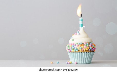 Birthday cupcake with pastel colored sprinkles and one birthday cake candle on a gray background with copyspace to side
