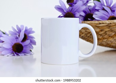 Cốc cà phê trắng bằng gốm với những bông hoa màu tím trong giỏ bằng liễu gai. Mockup cốc 11 oz trống để thiết kế.