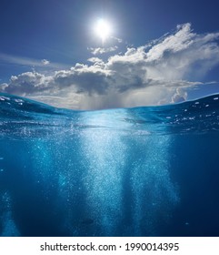 Meereslandschaft, Luftblasen unter Wasser und sonniger blauer Himmel mit Wolken, geteilter Blick über und unter der Wasseroberfläche