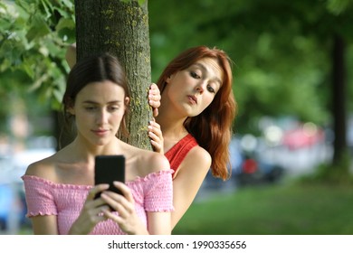 Afgeleide vrouw met behulp van slimme telefoon wordt bespioneerd door haar nieuwsgierige vriend in een park