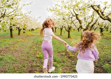 rear view. Two beautiful and happy girls run between the trees in the flowering spring garden. happy childhood. walks in outdoor parks. active games.