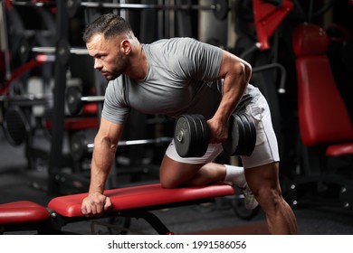 Bodybuilder doet halterrij voor rugtraining op een bankje in de fitnessruimte