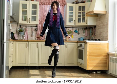 Cô gái tóc nâu trẻ đẹp trong bộ đồng phục của một nữ sinh Nhật Bản ở nhà trong nhà bếp trong tai nghe nhạc
