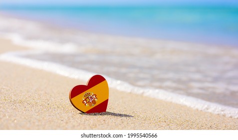 Flagge Spaniens in Form eines Herzens an einem Sandstrand. Das Konzept des besten Urlaubs in Spanien