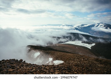 Stimmungsvolle Landschaft auf dem Gipfel eines Bergkamms über dicken, tief hängenden Wolken. Malerische Aussicht vom Rand des Abgrunds über Wolken auf schneebedeckte Berge. Wunderschöne Alpenlandschaft mit Gebirgskette über dichten Wolken.