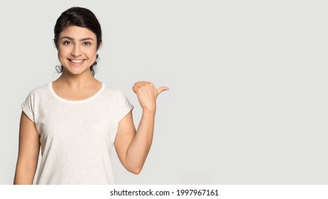 Porträt einer lächelnden indischen Frau isoliert auf grauem Studiohintergrund zeigen auf leeren leeren Kopierraum. Glückliche tausendjährige Mischlingsfrauen zeigen gute Werbeangebote oder Verkaufsrabatte. Handelskonzept.