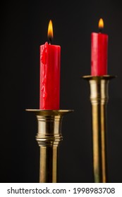 Gambar dekat dua lilin merah menyala dalam batang lilin emas, dengan fokus terpilih, latar belakang hitam, menegak