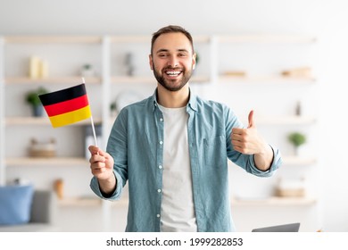 Happy Caucasian man showing thumb up and flag of Germany, posing and smiling at camera indoors. Cheerful millennial student recommending foreign education, learning German language