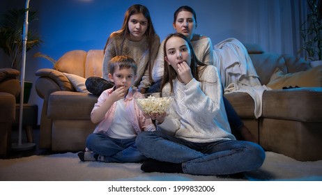 Group of people eating popcorn while watching movie or TV show in living room at night.