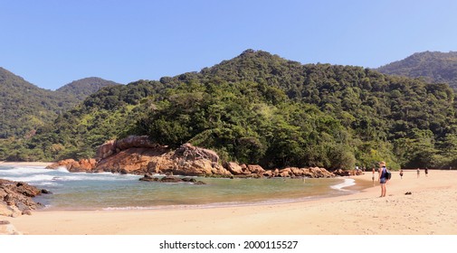 ブラジル、トリンダーデの美しいビーチでバックパックを持って立っている女性。背景には、植物が生い茂る山々。旅行者、人生を楽しむ、心の安らぎのコンセプト。