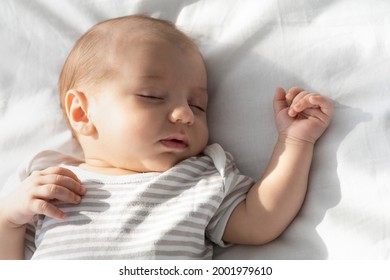 Tiempo de sueño diurno. Retrato de primer plano de un adorable bebé recién nacido durmiendo en la cama, un lindo y encantador niño pequeño con un mono a rayas acostado con una mano arriba, un niño o una niña durmiendo la siesta en casa, imagen recortada