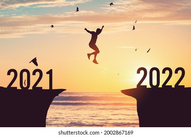 Silhouetmens die tussen klif springt met nummer 2021 tot 2022 en vogels die vliegen op tropisch zonsondergangstrand. Vrijheidsuitdaging en reisavontuurvakantieconcept. Vintage toonfilter effect kleurstijl.