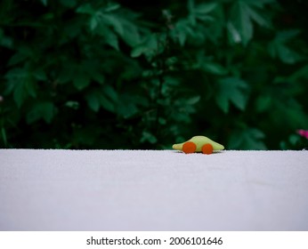 Coche de juguete de arcilla presentado en superficie blanca con fondo borroso de hojas verdes.