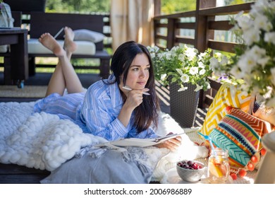 Mujer morena enfocada pensando en la imaginación con bolígrafo y bloc de notas en la terraza del pueblo al aire libre de verano de la naturaleza. Mujer asiática pensativa tomando notas escribiendo un diario de papel relajándose en el balcón de la casa de campo